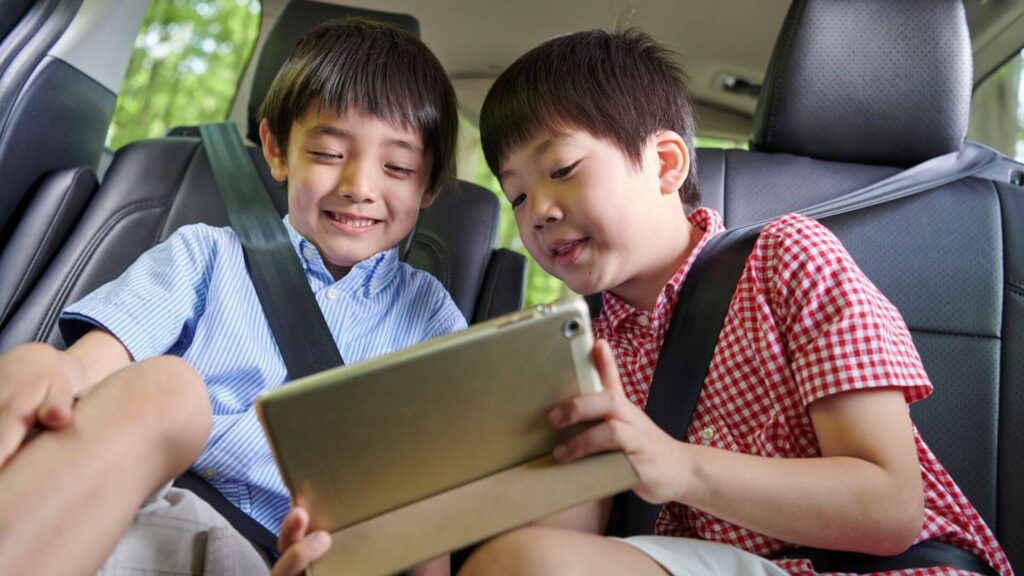 NorthSiginal Two boys sitting in the back seat of a car, wearing seatbelts and enjoying a tablet together, connected with North Signal Wifi Rental. Starlink Rental